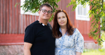 Pasi ja Asako Palmu seisovat punaiset puutalon edessä.