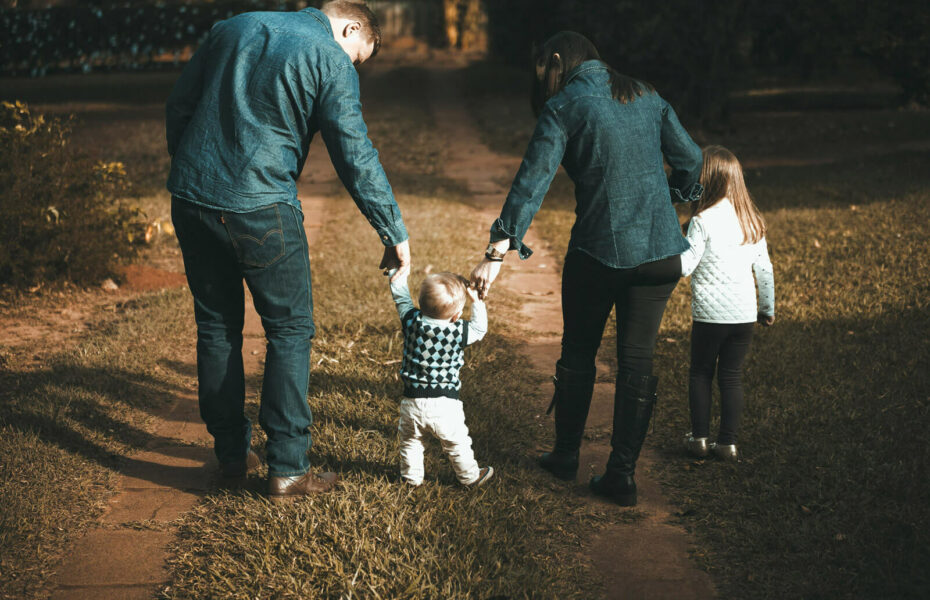 Äiti ja isä ja kaksi lasta kävelevät hiekkatietä.