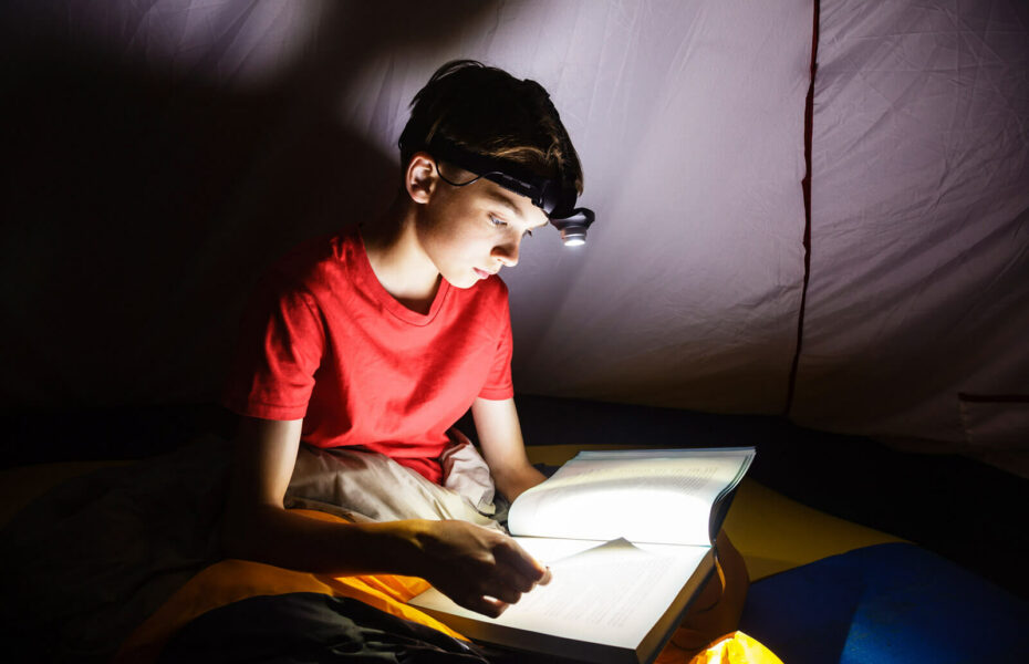 Poika lukee kirjaa otsalampun valossa.