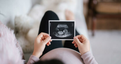 Raskaana oleva nainen katselee käsissään olevaa ultrakuvaa vauvasta.