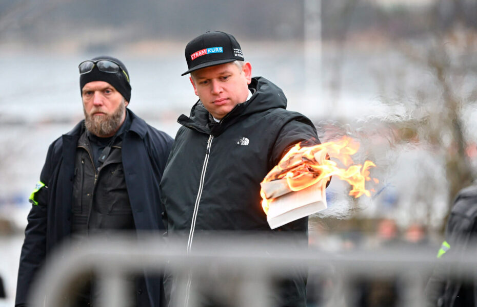 Rasmus Paludan pitää kädessään palavaa Koraania. Hänen vieressään seisoo toinen mies.