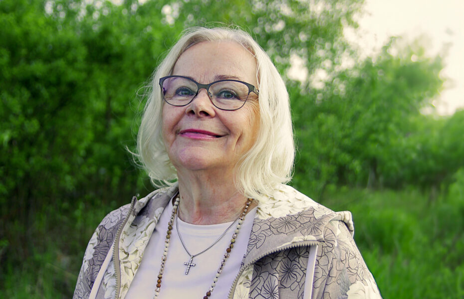nainen hymyilee luonnon keskellä.