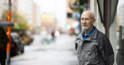 Valkopartainen mies seisoo kadulla ja katsoo kaukaisuuteen.