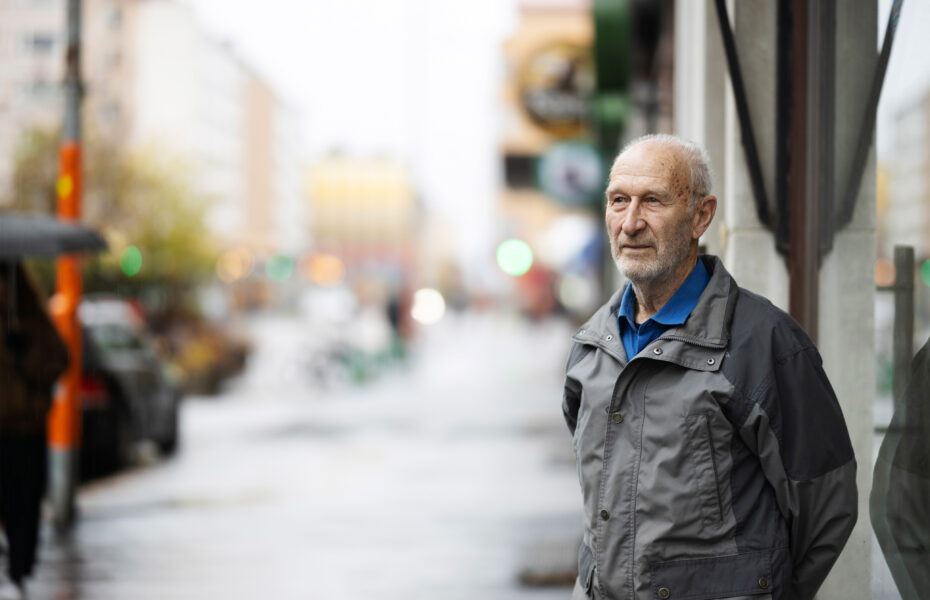 Valkopartainen mies seisoo kadulla ja katsoo kaukaisuuteen.