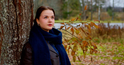 Nainen, joka nojaa puuhun.