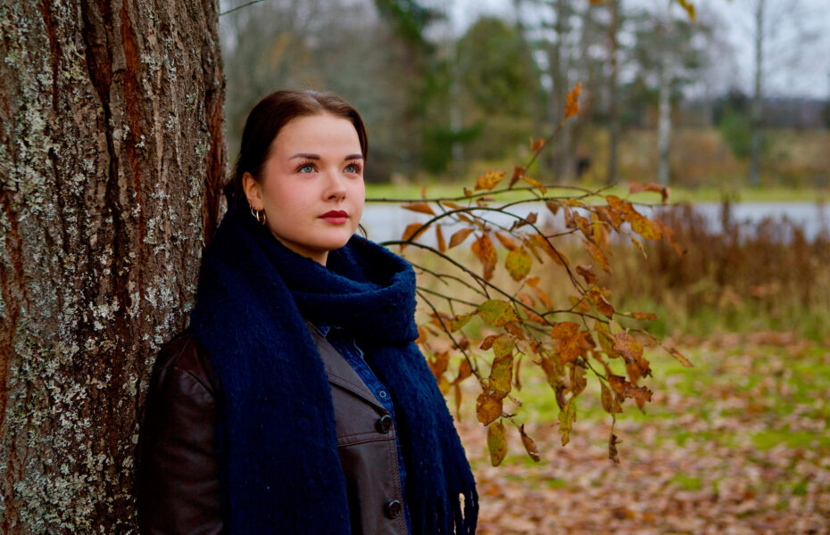 Nainen, joka nojaa puuhun.