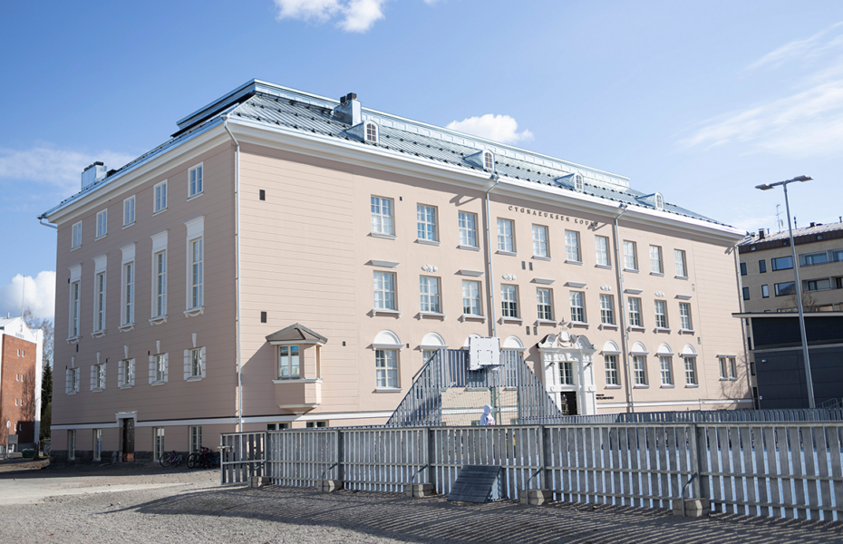 Iso kolmikerroksinen koulurakennus. Vieressä koripallokenttä.