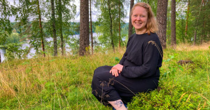 Nainen istuu metsässä ja nauraa.