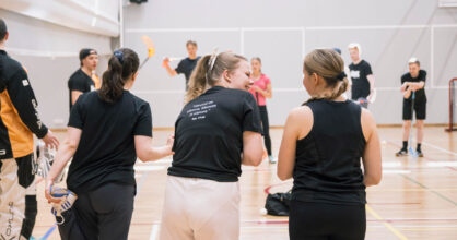 Naiset seisoskelevat sählykentän reunassa ennen pelin alkua.