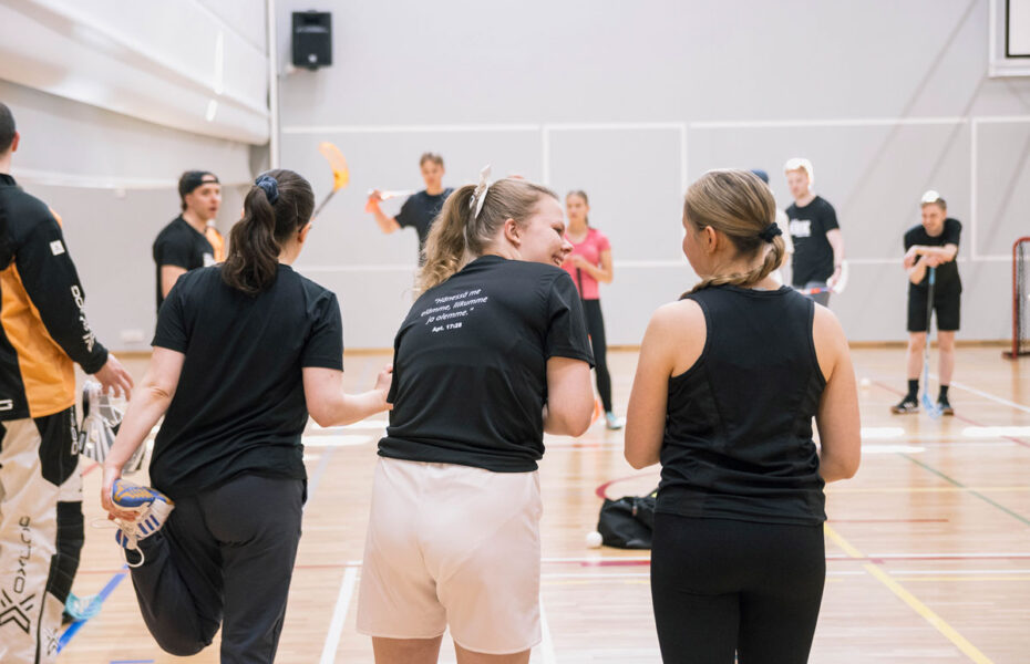 Naiset seisoskelevat sählykentän reunassa ennen pelin alkua.