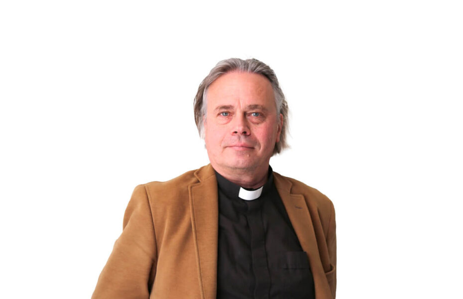 Harmaahiuksisella miehellä on papinpaita ja ruskea takki.