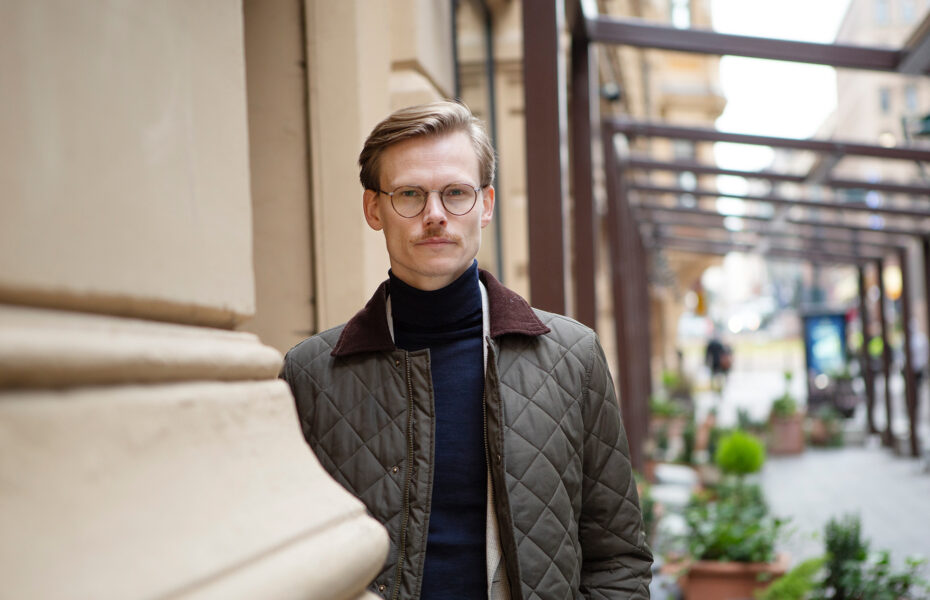 Mies seisoo kaupungin kadulla silmälaseissa takki päällä.