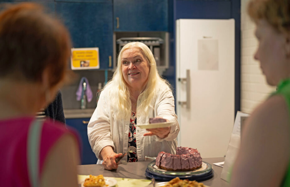 Seija Nurmi tarjoaa pöydän yli laustasta, jossa on kakun palanen. Hänellä on vaaleat pitkät hiukset.