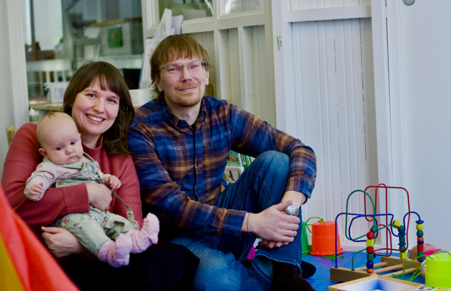 Kia ja Markus Syrjätie istuvat leikkihuoneen lattialla. Kialla on sylissä vauva.