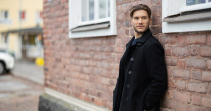 Mies nojaa tiilitalon seinään ulkona ja katsoo sivulle.