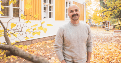 Mies poolopaidassa hymyilee ja pitää käsiään taskussa. Taustalla ruskaa.