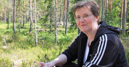 Nainen istuu metsän kupeessa.