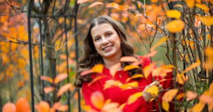 Nuori nainen hymyilee lehtipuiden keskellä.