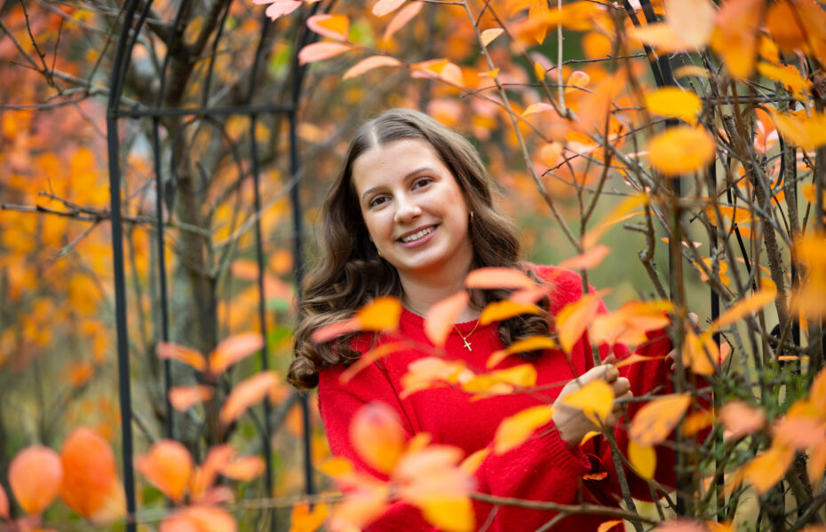 Nuori nainen hymyilee lehtipuiden keskellä.