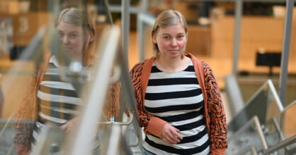 Tanja nojaa portaan kaiteeseen ja hymyilee. Hänellä on polkkamittainen vaalean ruskea tukka.