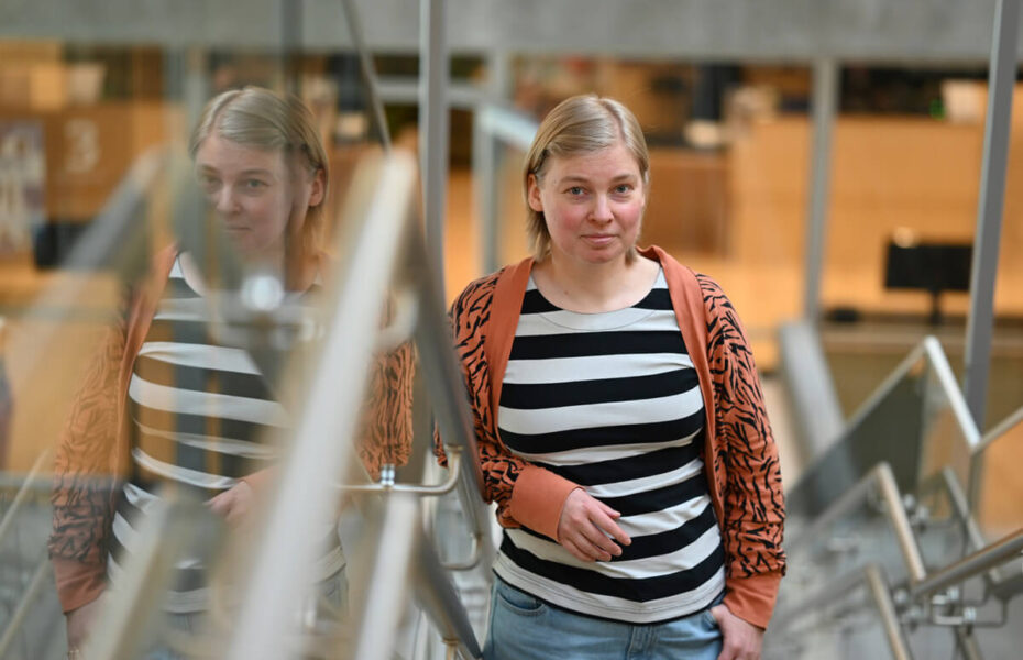 Tanja nojaa portaan kaiteeseen ja hymyilee. Hänellä on polkkamittainen vaalean ruskea tukka.