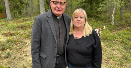 Mies pappispuvussa ja hänen vaaleahiuksinen vaimo poseeraa taustalla metsää.