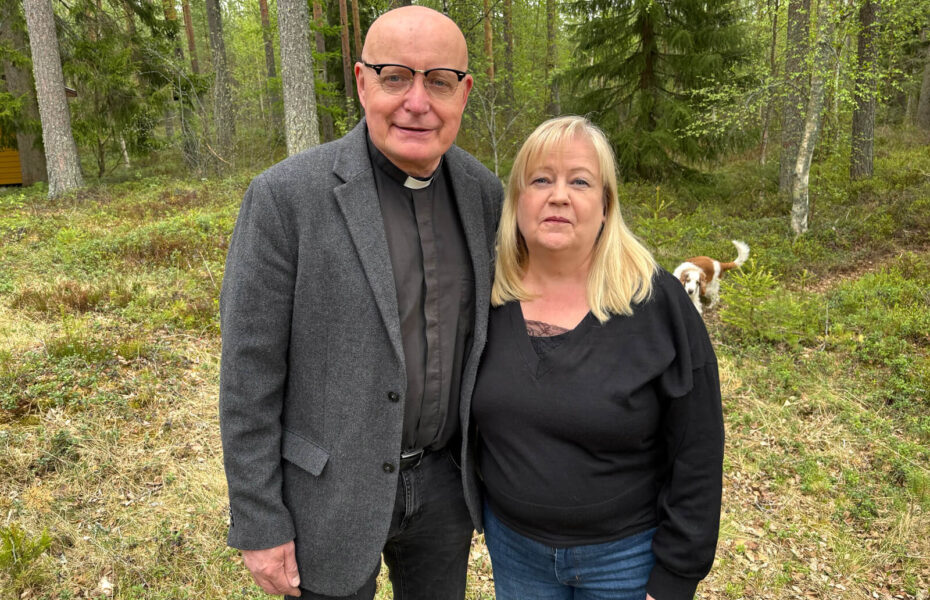 Mies pappispuvussa ja hänen vaaleahiuksinen vaimo poseeraa taustalla metsää.