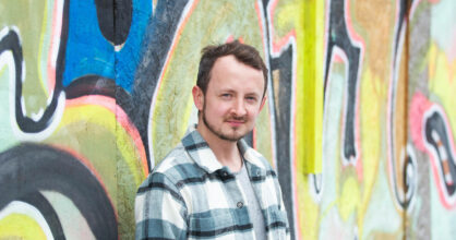 Tero Huuskonen seisoo graffiittimaalatun seinän edessä.