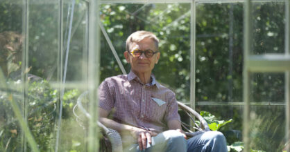 Timo Junkkaala istuu puutarhassaan ja katsoo kameraan.
