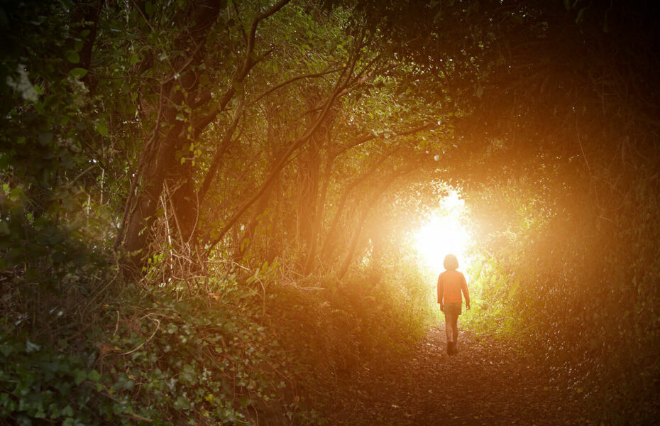 Tyttö kävelee metsässä kohti valoa.