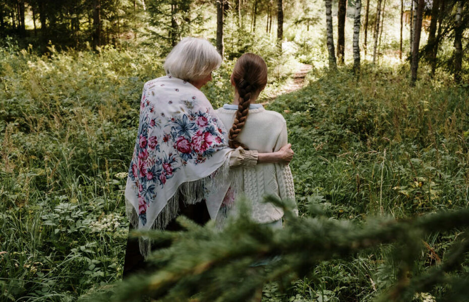 Vanha ja nuori nainen seisovat vierekkäin metsässä. Vanha nainen lohduttaa nuorempaa.