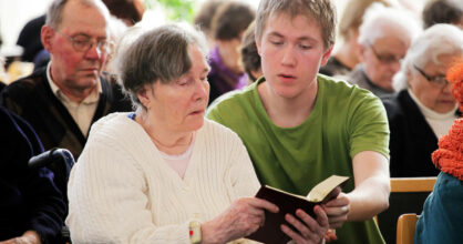 Nuori poika lukee virsikirjaa yhdessä iäkkään naisen kanssa.