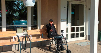 Iäkäs mies istuu penkillä. Hänen edessään on rollaattori.