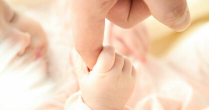 Vauva pitää aikuisen sormesta kiinni.
