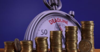 kolikkopinoja, joiden takana on kello, joka osoittaa deadlinea