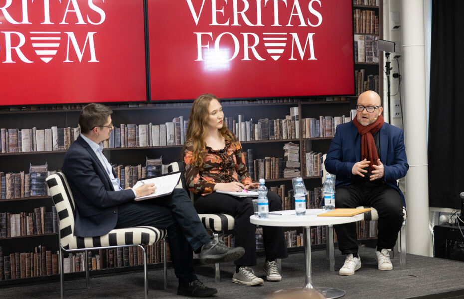 Kaksi miestä ja yksi nainen istuvat pöydän ääressä ja keskustelevat