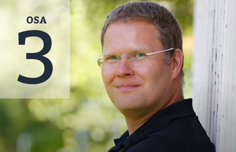 Mies nojaa seinään ja katsoo kohti. Silmälasit ja lyhyet hiukset.
