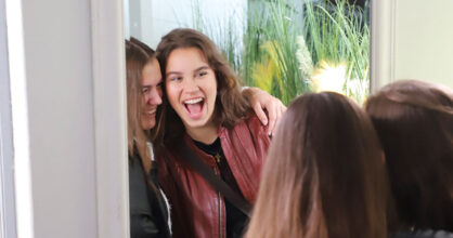 Kaksi tyttöä katsoo toisiaan peilistä ja nauraa.