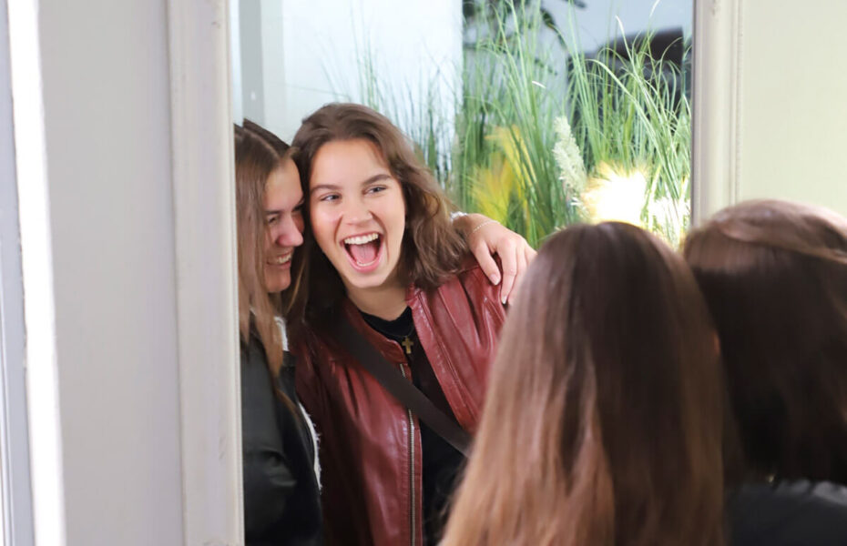 Kaksi tyttöä katsoo toisiaan peilistä ja nauraa.